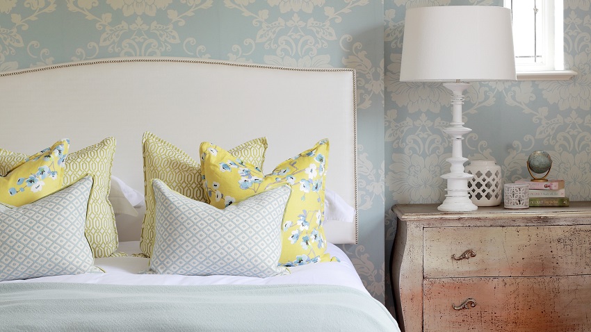 Floral, pastel blue wallpaper and rug combined with timeless mixture of patterns on scatter cushions on double bed